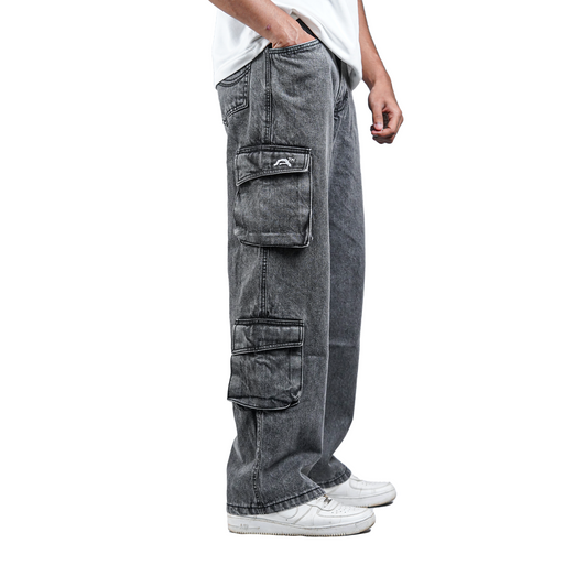 Model wearing grey denim cargo with embroidery insanity trademark facing side to the camera with all white background with hands in the pocket white tshirt and white shoes 
